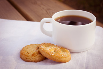 Cup of coffee with cookies on cloth and wooden table.