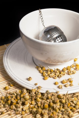 Dry chamomile with tea strainer in a cup of hot water
