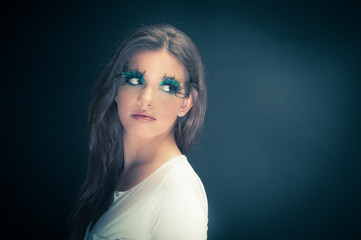 Young woman in the studio with extreme makeup against dark backg