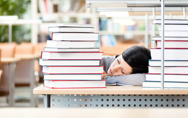 Female student sleeping at the desk with piles of books