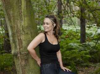 Fototapeta premium attractive woman in woodland setting leaning against a tree