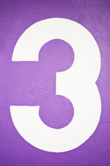 Zahl Drei auf lila Wand
