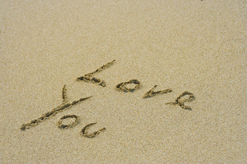 Conceptual handwritten love you text in sand