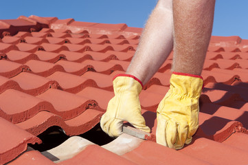 Worker repairing roof tiles on house