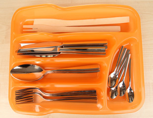 Orange plastic cutlery tray with checked cutlery on wooden