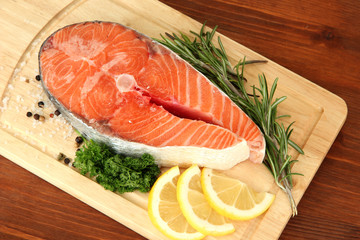 Fresh salmon steak on cutting board, on wooden background