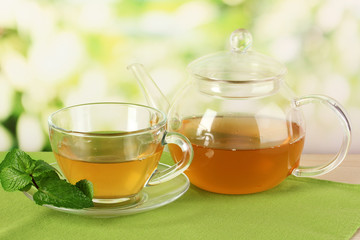 Cup of tea with mint on table on bright bacground