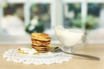 Sweet pancakes on plate with sour cream on table in kitchen