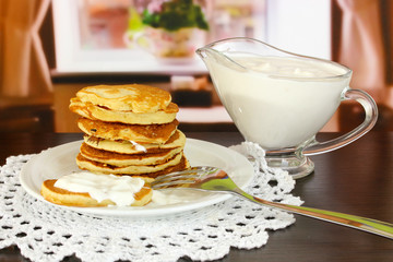Sweet pancakes on plate with sour cream on table in room