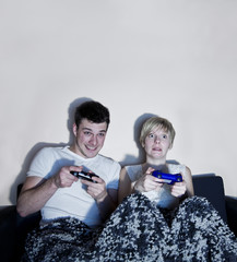 Young couple playing video games comfortably wrapped in a blanke