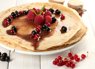Delicious pancakes with berries and jam on plate on wooden