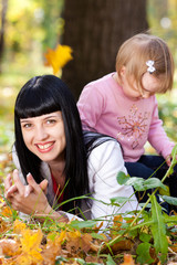 beautiful young mother and her daughter lying on the autumn leav