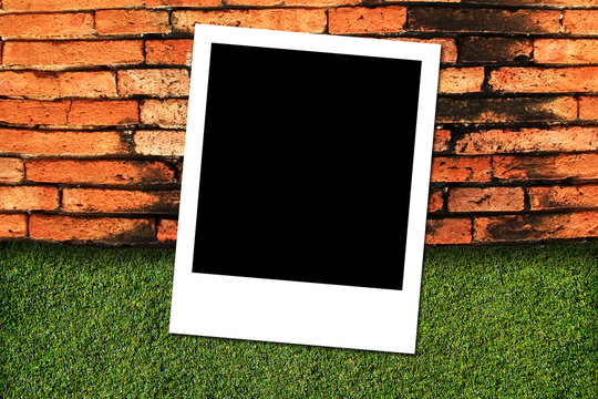 Photo frame on green grass and brick wall