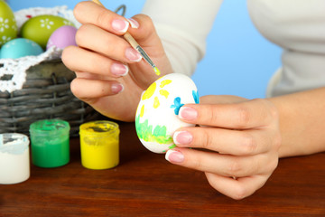 Young woman painting Easter eggs, on color background