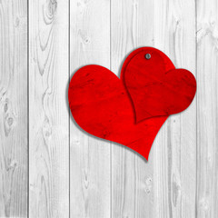 Conceptual two red old paper vintage hearts nailed on white wood
