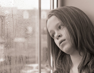 A young girl gazing out of a window on a rainy day