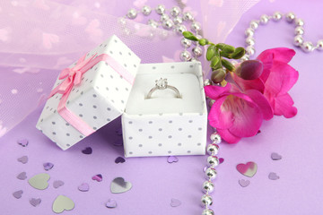 Beautiful box with wedding ring and flower on purple background