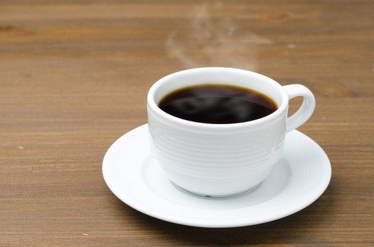 cup of black coffee with steam on a brown wooden table