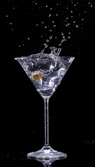 Martini drink splashing out of glass on black background