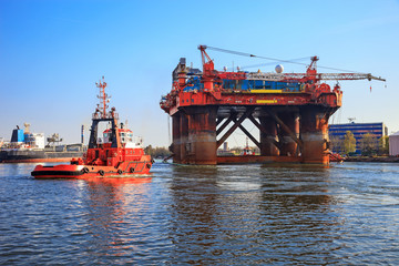 Oil rig in the company of a tug boats enters a port.