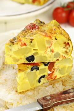 Slices of Spanish potato tortilla with black olives and tomatoes