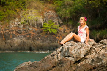 Beautiful blonde on a rock by the sea.