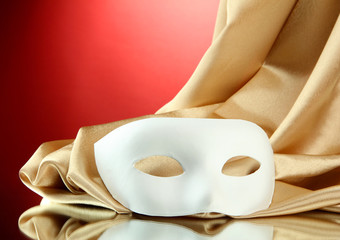 White mask and golden silk fabric, on red background