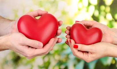 Fototapeta na wymiar Red hearts in woman and man hands, on green background