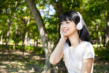 Naklejka premium atractive asian woman listening music in the park