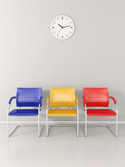 A wall clock and 3 colored chairs in the waiting room