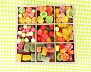 Multicolor candies in wooden box, on color background