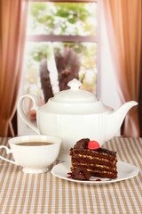 Teapot, cup of tea and delicious cake on window background