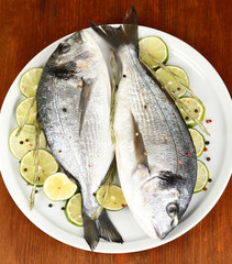 Two fish dorado with lemon on plate on wooden table close-up