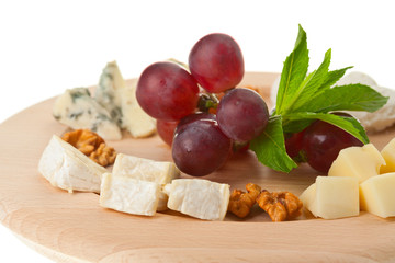 Various types of cheese with nuts and grapes on plate