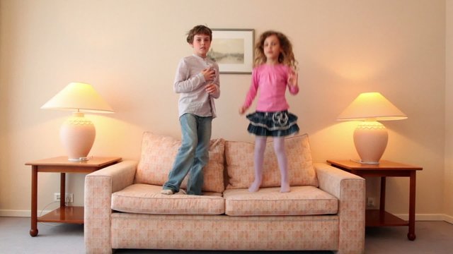 Two kids jump on sofa and then run away from room with lamps on