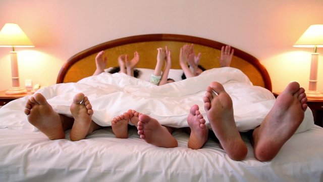 Family makes various gestures by hands in bed under white