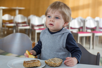 Little boy with eating bread and apple in kindergarten