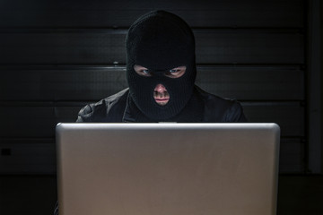 masked hacker sitting behind compuiter