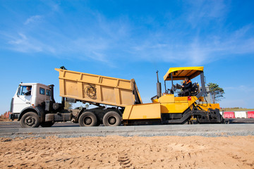 Tipper unloading fresh asphalt from body into tracked paver