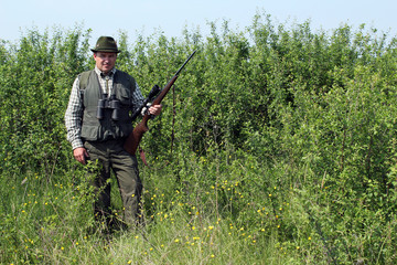 hunter with rifle standing in bush