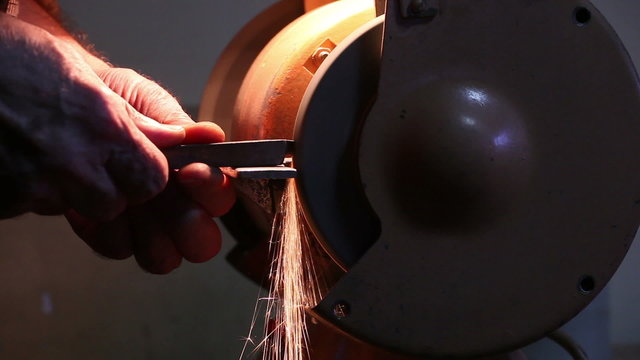 worker sharpens metal piece on the abrasive machine 1
