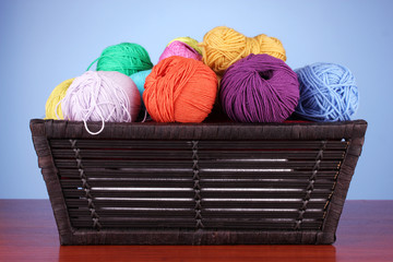 Colorful yarn balls in basket on color background