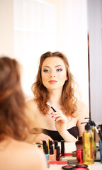 Young beautiful woman making make-up near mirror