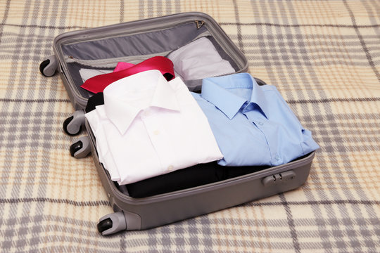 Open grey suitcase with clothing on plaid