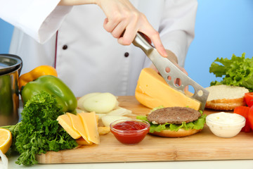 Female hands preparing cheeseburger, on blue background