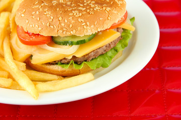 Tasty cheeseburger with fried potatoes, on red background