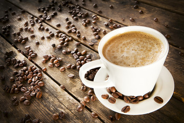 A cup of coffee surrounded by coffee beans.