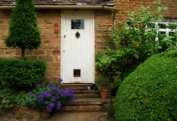Fototapeta na wymiar White wooden country house door, stonewall, plants