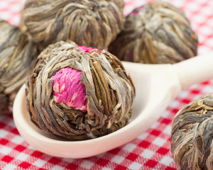 Green tea balls with flowers in wooden spoon on kitchen table