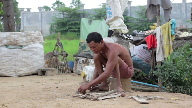 Father in slums preparing fire by cutting wood